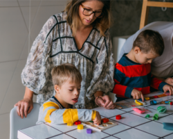Two children with Down syndrome joyfully assemble puzzles under the guidance of an attentive adult.