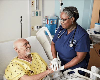 Male patient in bed with female staff member standing over his bed at MLK Community Healthcare Center. Both people are smiling