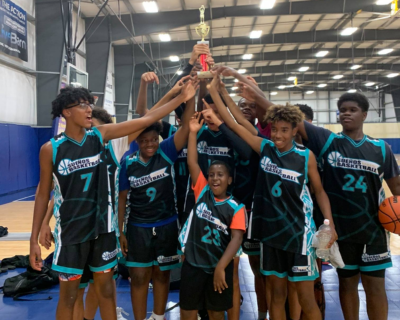 A jubilant youth basketball team in teal and black jerseys raising a championship trophy together on an indoor court, exemplifying teamwork and achievement.