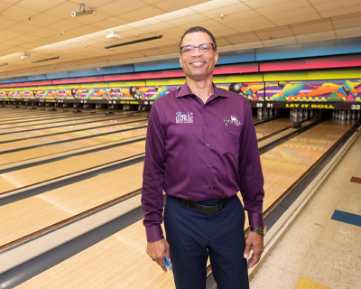 Stacy Anderson standing proudly in the Let it Roll Bowl alley with bowling lanes in the background.