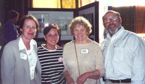 Group photo of four individuals at a social event. From left to right, a woman named Marla, a woman named Kim, a woman named Natalie Kennedy, and a man named Allen P. Baldwin. They are all smiling and looking towards the camera. The name tags on their clothing are visible, and a bright window forms the background.