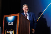 A smiling man with glasses speaking at the podium during the Clearinghouse CDFI 2024 Annual Shareholders Meeting.