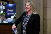A happy woman standing next to an 'Open Bar' sign at the Clearinghouse CDFI 2024 Annual Shareholders Meeting