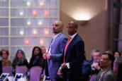 Two men, one in a purple tie and the other in a red tie, standing attentively at the Clearinghouse CDFI event