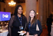 Two women, one with a name tag reading 'Shannon Lawrence', smiling at the camera with a conference setup in the background