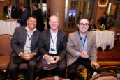Three seated men in business attire, enjoying a moment together, with a conference background at the Clearinghouse CDFI event