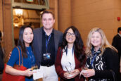 our individuals, one woman and three men, enjoying a conversation with drinks in their hands at the meeting. They all have conference ID tags and are dressed in business casual attire.