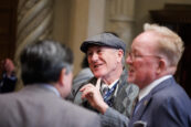 An attendee in a classic tweed cap and a patterned scarf listens intently during a casual group discussion at the Clearinghouse CDFI's shareholders meeting