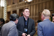 A young professional in a black jacket and blue shirt stands out in a crowd of shareholders engaged in conversation at the Clearinghouse CDFI meeting