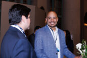 A smiling gentleman in a gray suit engages in conversation with another attendee at the Clearinghouse CDFI's 2024 Annual Shareholders Meeting.