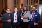 Group of four professionals chatting and holding drinks at a Clearinghouse CDFI networking event, with others in the background