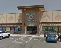 Front view of the Wa-She-Shu Travel Plaza on a sunny day, featuring parked cars, shoppers, and distinct tribal design elements on the façade