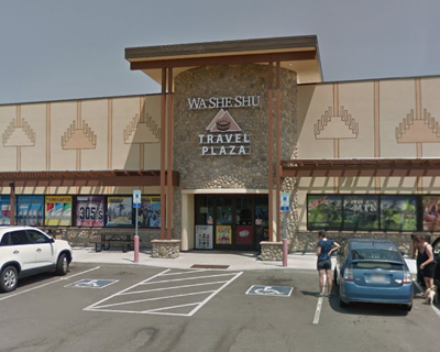 Front view of the Wa-She-Shu Travel Plaza on a sunny day, featuring parked cars, shoppers, and distinct tribal design elements on the façade