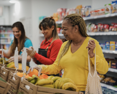 Three diverse women shopping for fresh fruits and vegetables in a grocery store aisle, emphasizing community and healthy choices