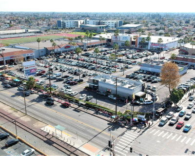 Aerial view of a busy shopping center with a large parking lot, multiple retail stores, and a bustling street in the foreground.
