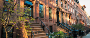 Charming row of brownstone townhouses in Prospect Lefferts Gardens, Brooklyn, bathed in warm sunset light, highlighting their ornate architectural details and inviting stoops adorned with greenery.