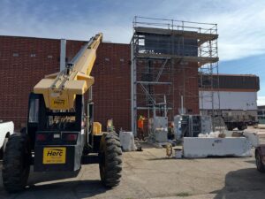 Construction site of the new Kolar Family YMCA in Downey, CA, with scaffolding, workers, and heavy equipment.