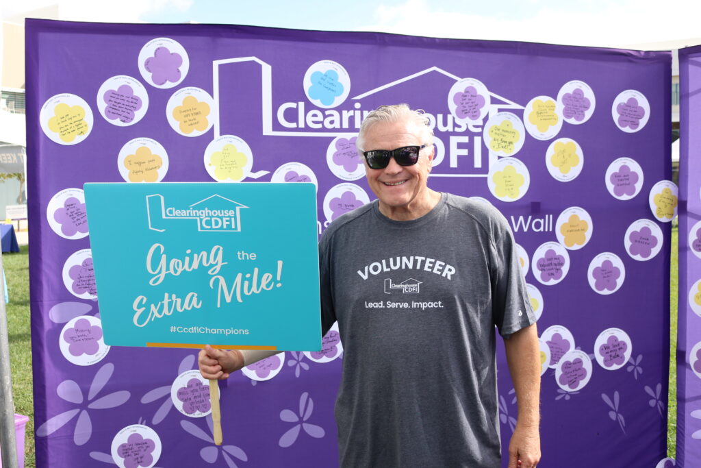 Clearinghouse CDFI President and CEO at the 2025 Walk to End Alzheimer’s, standing before the CCDFI Message of Hope wall holding a sign that reads “Going the Extra Mile.”