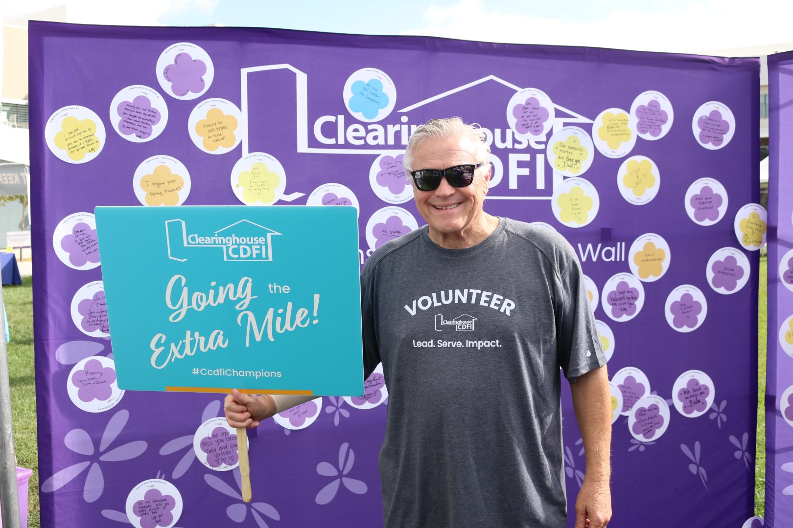 Clearinghouse CDFI President and CEO at the 2025 Walk to End Alzheimer’s, standing before the CCDFI Message of Hope wall holding a sign that reads “Going the Extra Mile.”
