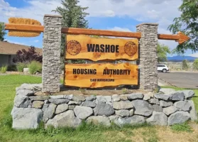 Entrance sign for the Washoe Housing Authority with stone pillars and carved wooden panels, set on a landscaped lawn under a partly cloudy sky.