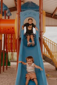 Two young children sliding down colorful slide with smiling faces, representing Clearinghouse CDFI's mission-driven lending philosophy