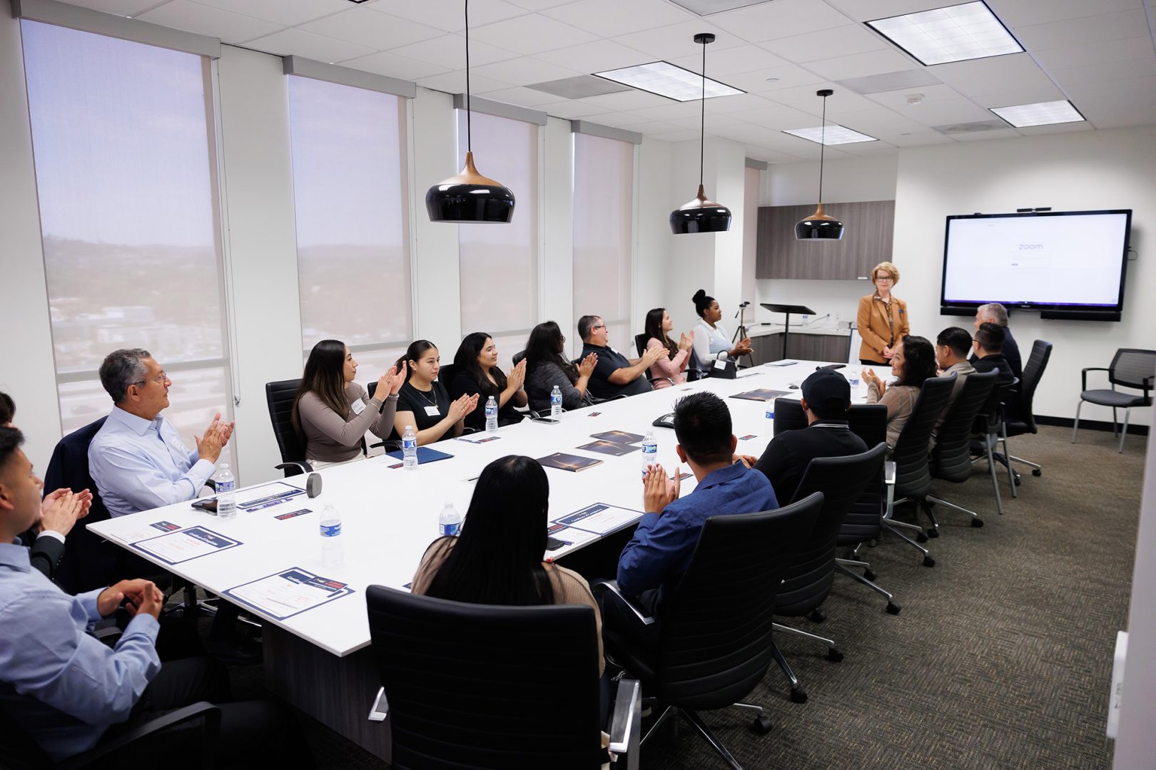 Clearinghouse CDFI 'B' BOLD intern cohort sitting around conference room table, clapping after presentation from Internship Director Susan Montoya