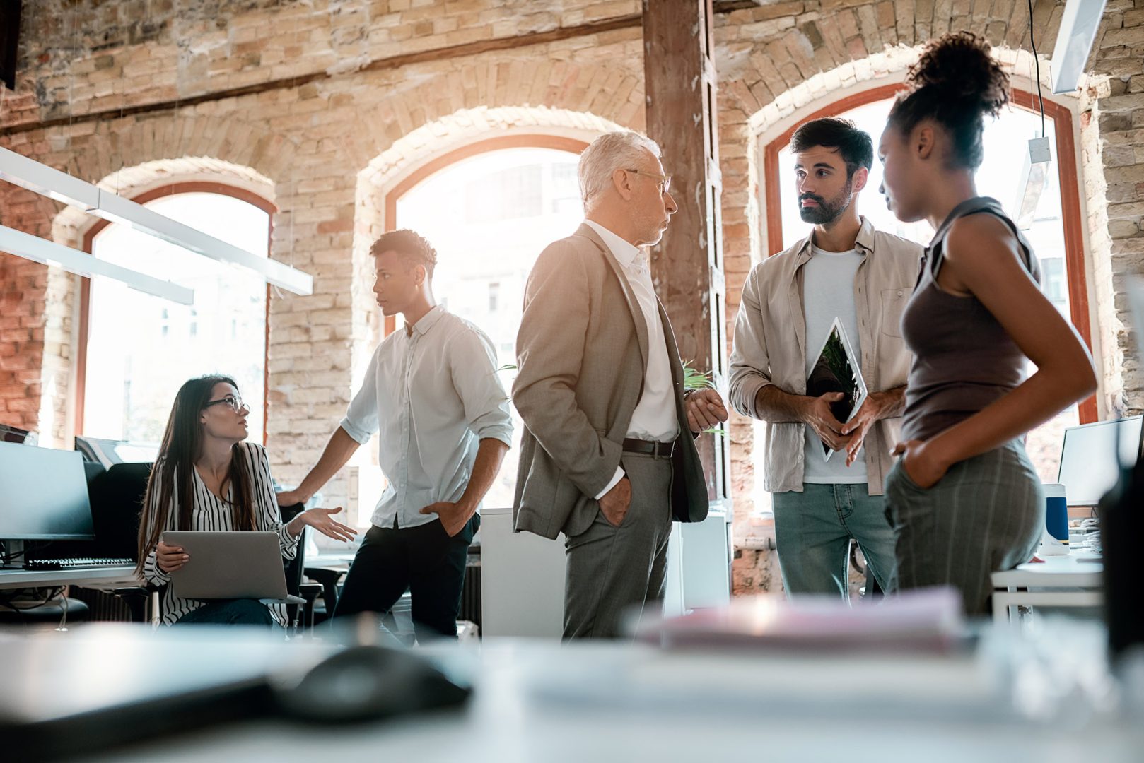Team members, including executive, standing in brick room with wooden beams having a discussion
