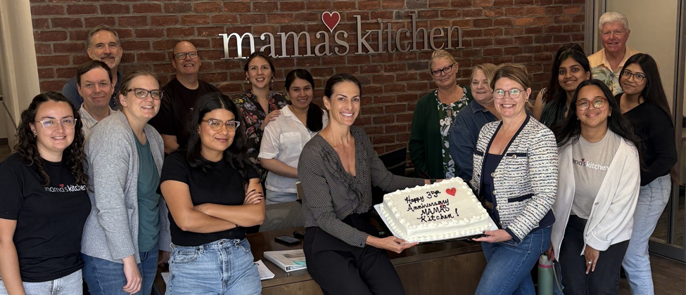 Team members at Mama’s Kitchen standing in front of organization logo inside nonprofit office
